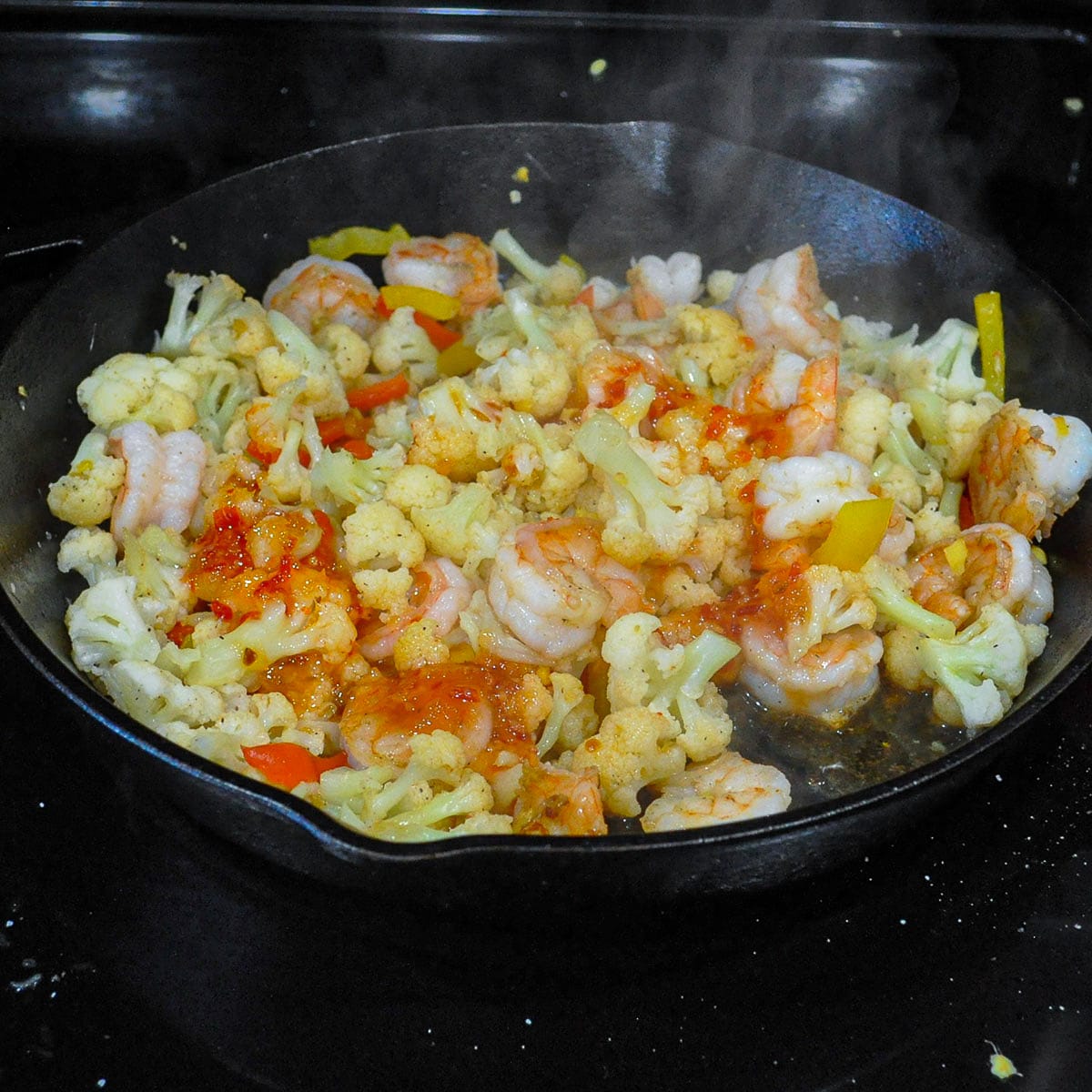 thai chili sauce poured over cauliflower and shrimp in a skillet
