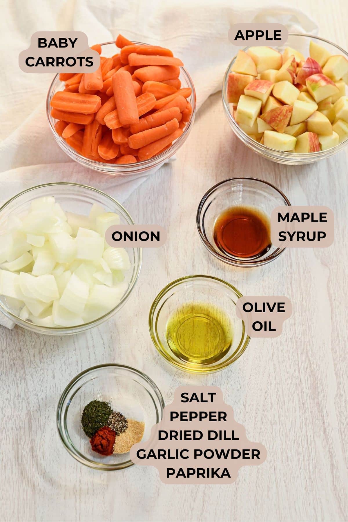 Bowls of Baby Carrots with Apples and Onions, maple syrup, olive oil, and spices arranged on a table.
