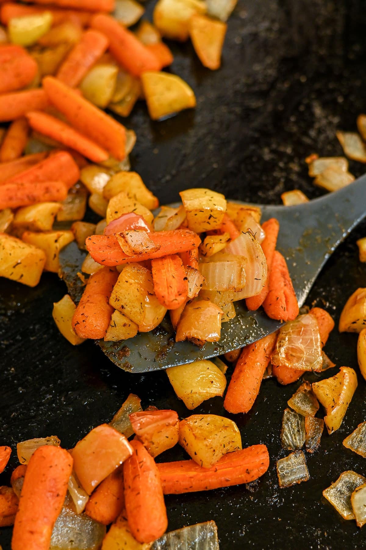 Spatula lifting Roasted Carrots with Apples and Onions from a baking sheet with more veggies scattered around.