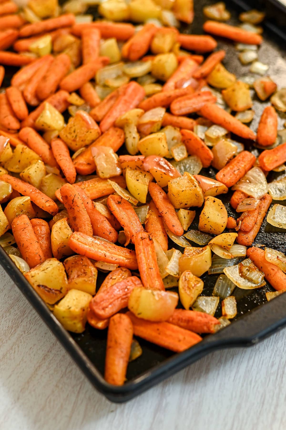 Roasted carrots with apples and onions, plus potatoes and herbs, on a black baking tray.