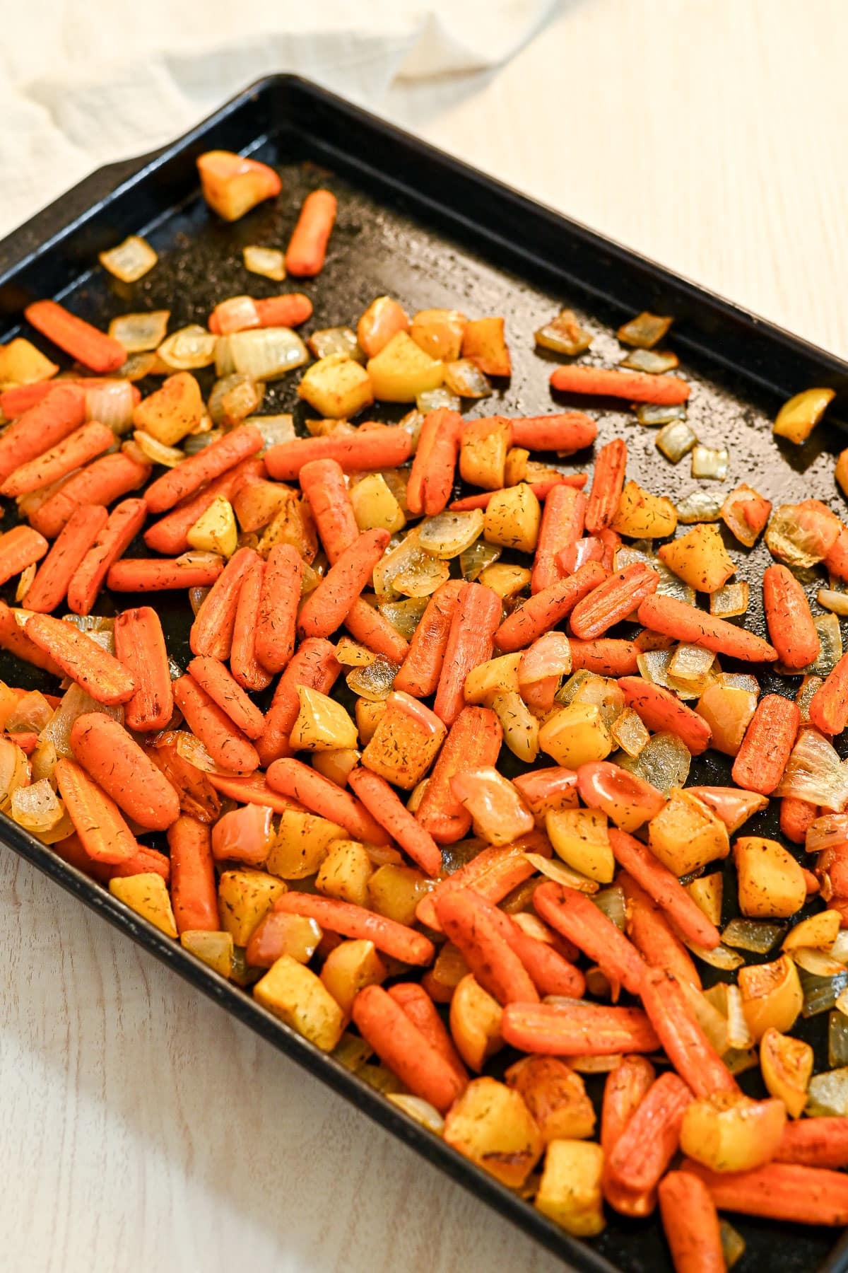Roasted Carrots with Apples and Onions on a black baking tray over a light wooden surface.