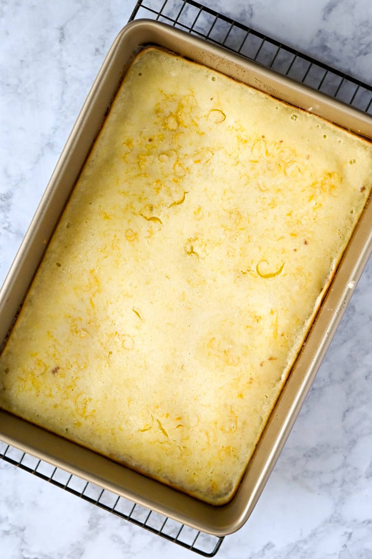 A pan of freshly baked Tart Lemon Bars cooling on a wire rack, with visible lemon zest on top.