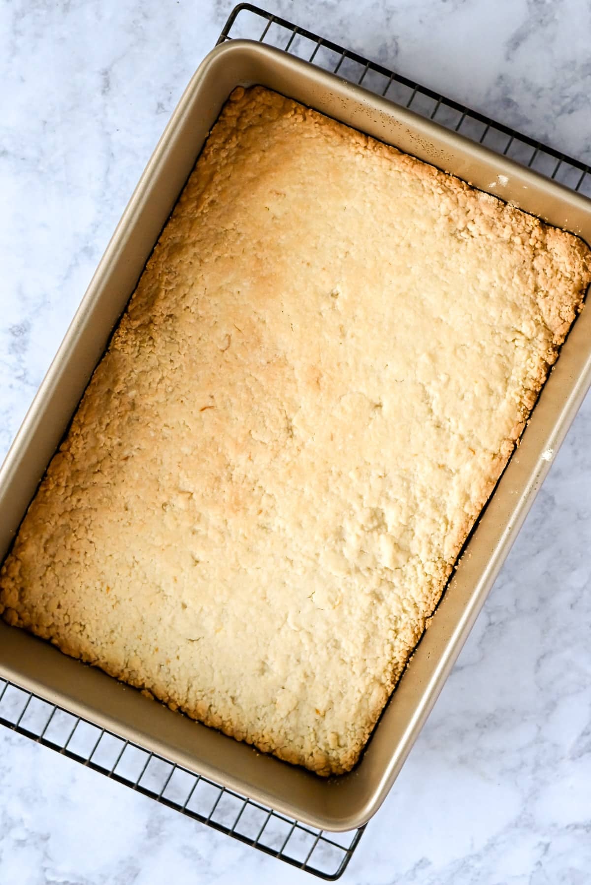 Golden, baked cake in a rectangular pan on a wire rack, set on a light marble surface-evoking the bright allure of tart lemon bars.