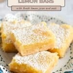 Four Tart Lemon Bars, dusted with powdered sugar, are stacked on a plate with a lace paper doily—an irresistible treat for fans of lemon cookies.