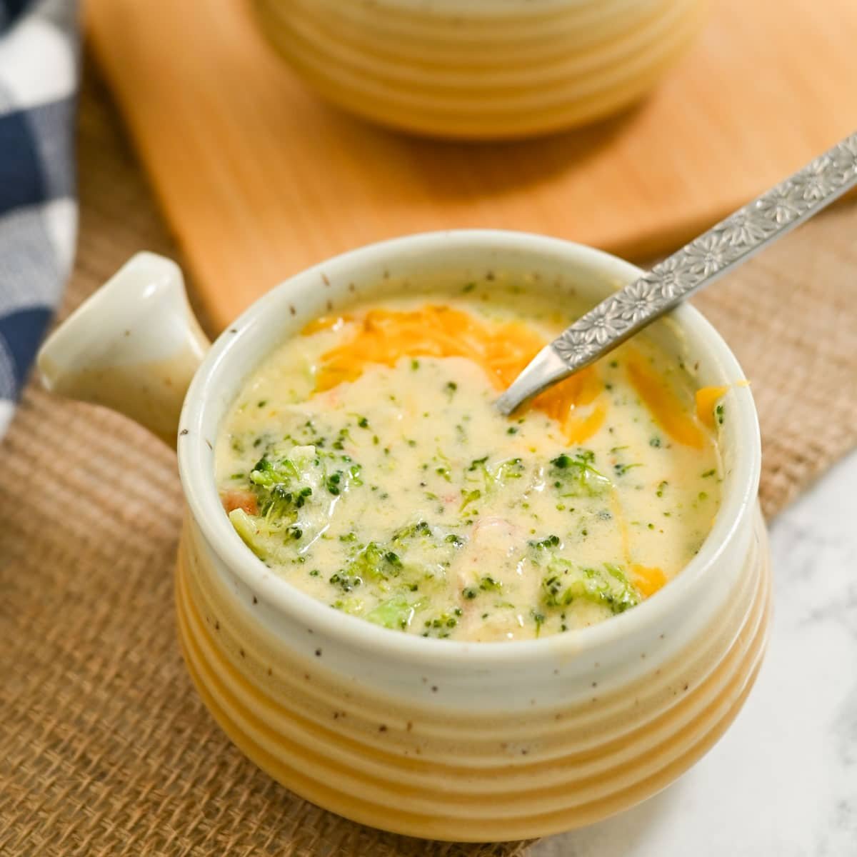 A steaming bowl of creamy broccoli cheese soup sits invitingly on a woven mat, with a spoon ready to dive in.