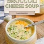 A bowl of creamy Broccoli Cheese Soup with a spoon, topped with melted cheese and served on a woven mat.