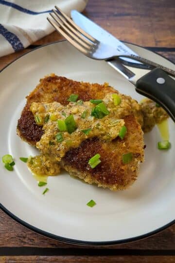 A panko pork chop topped with Dijon sauce on a plate with a knife and fork.