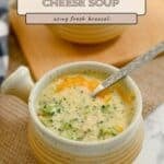 A comforting bowl of Broccoli Cheese Soup with a spoon, served on a woven mat beside a wooden board with crackers.