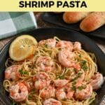 A plate of lemon shrimp spaghetti garnished with parsley, accompanied by a slice of lemon and breadsticks.