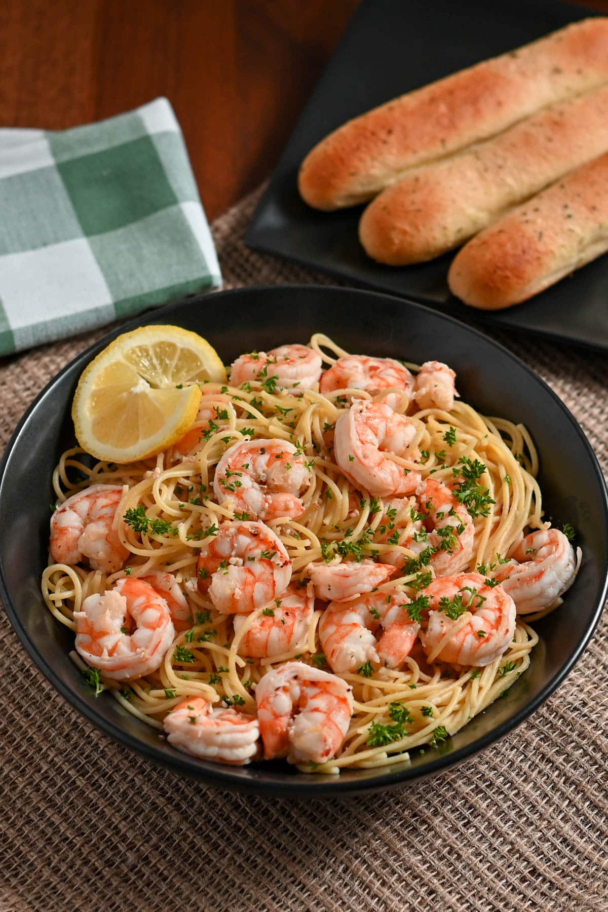 A plate of lemon shrimp pasta garnished with parsley and lemon, accompanied by breadsticks on a wooden table.