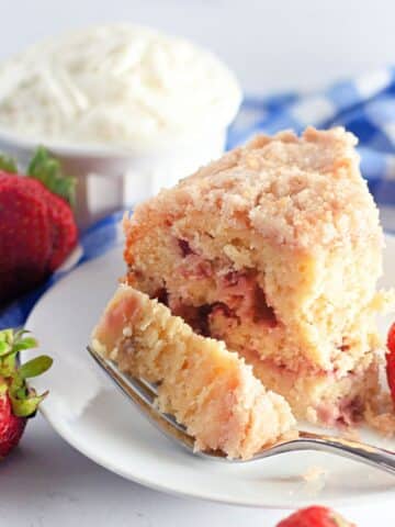 A slice of strawberry coffee cake on a white plate next to whipped cream and strawberries.