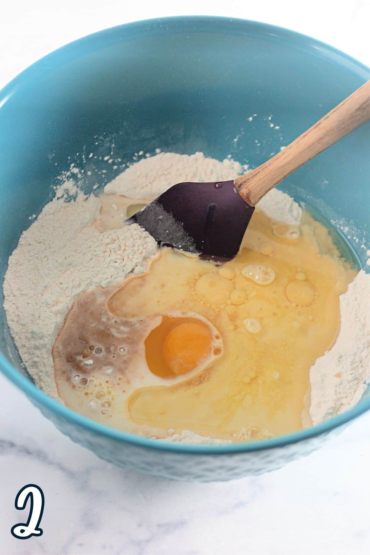 Egg, milk, juice, and other wet ingredients added to flour in a mixing bowl. 