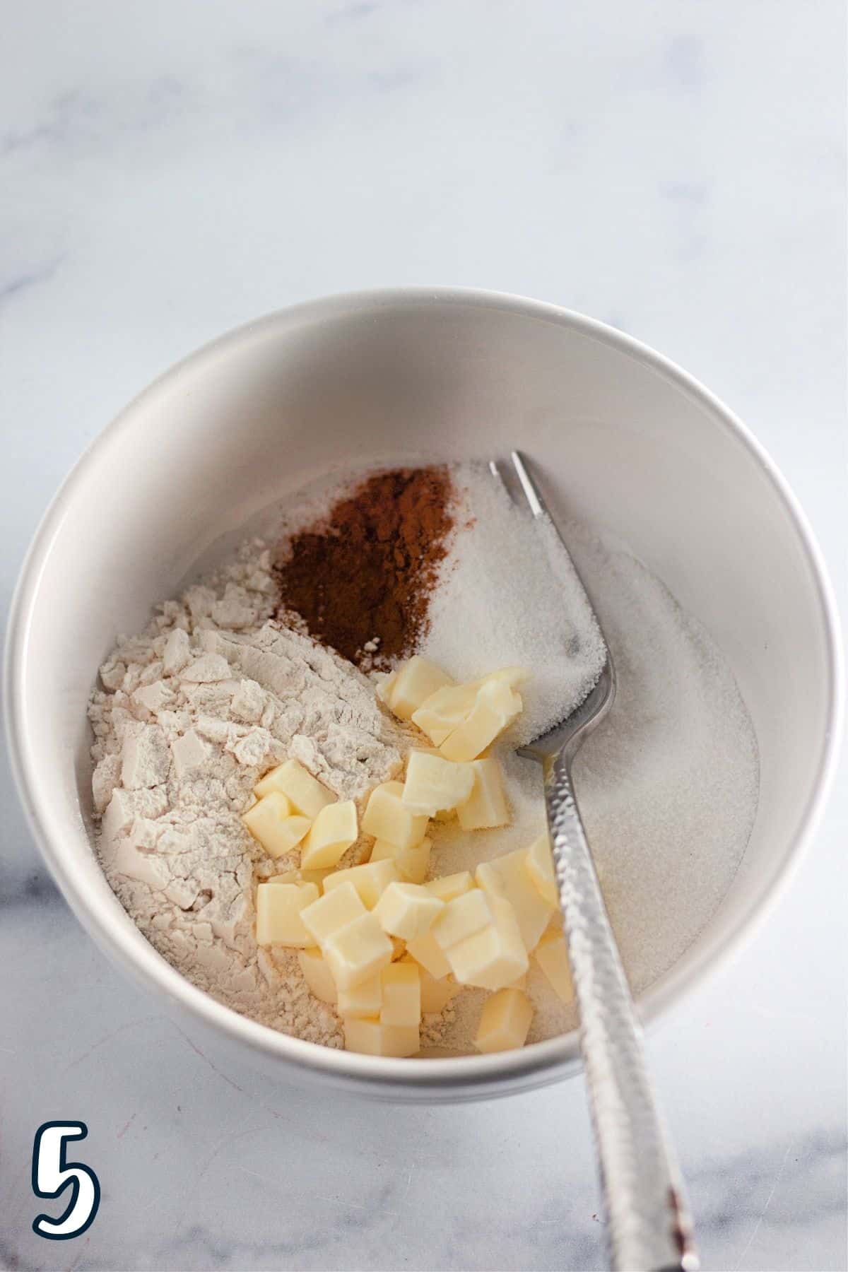 Flour, butter, sugar, and cinnamon in a white mixing bowl. 