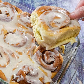 a cinnamon rolls being removed from the baking dish