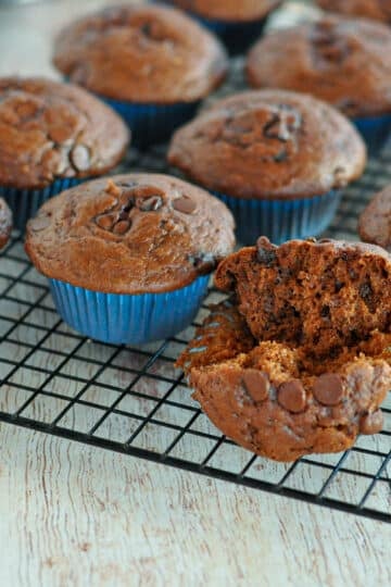 a spilt open muffin sitting on a wire rack next to other muffins.