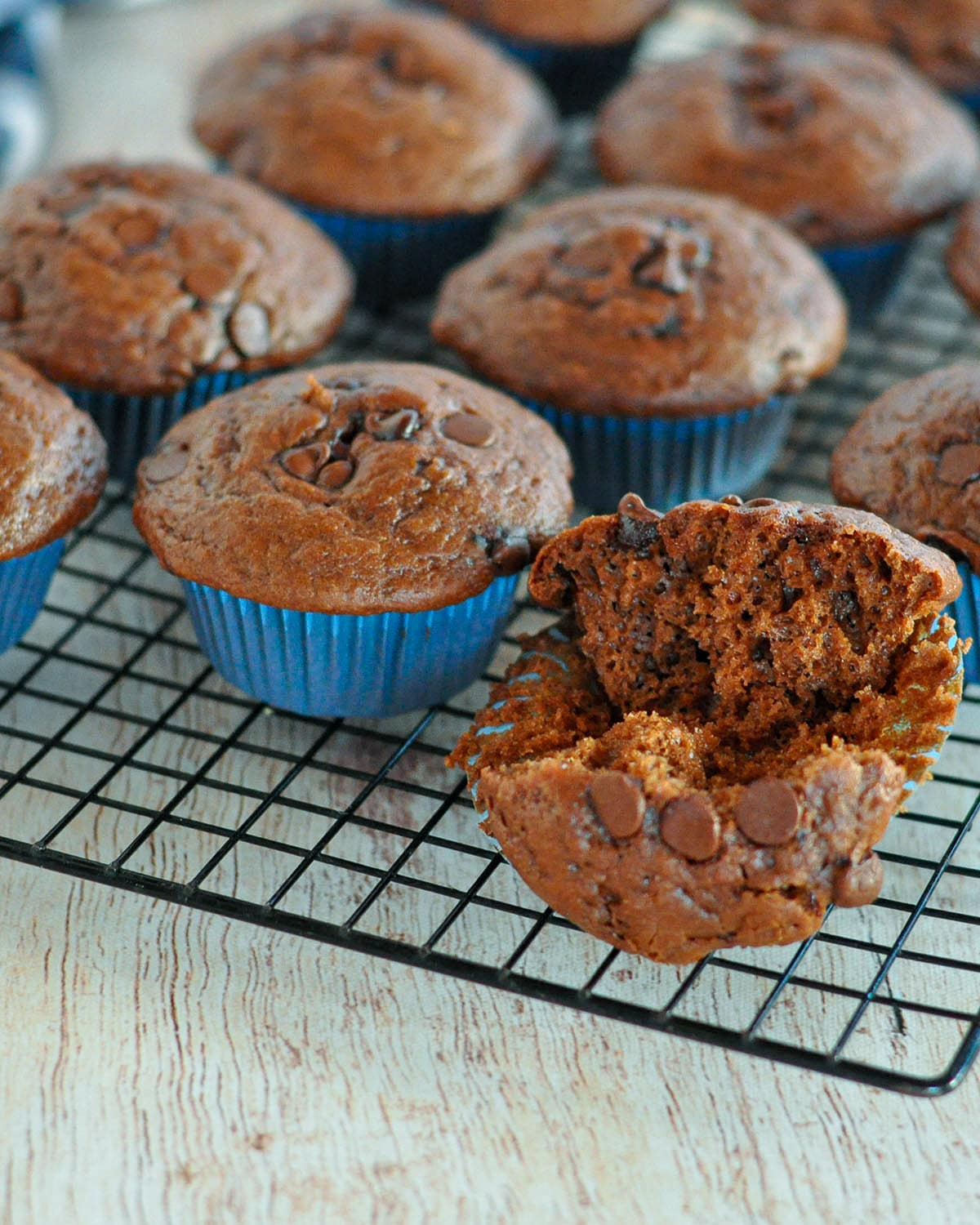 a spilt open muffin sitting on a wire rack next to other muffins. 