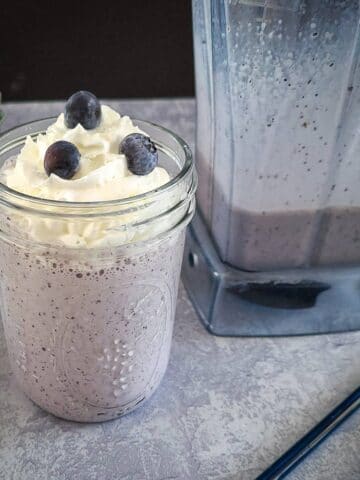 blueberry milkshake in a mason jar next to fresh berries and a blender.