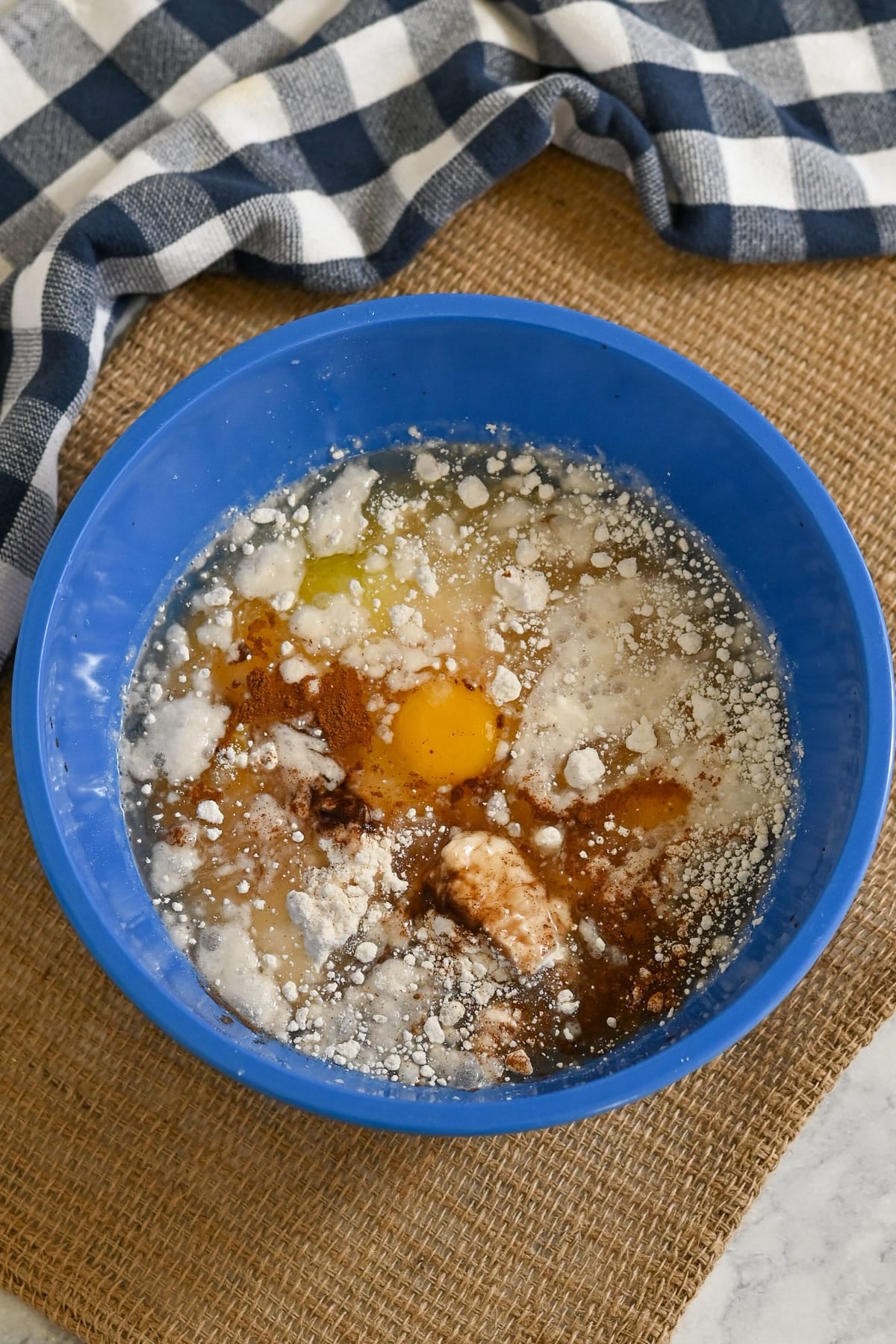 A blue bowl with flour, eggs, cinnamon, and other ingredients, ready to be mixed for baking a delicious Peaches and Cream Poke Cake.