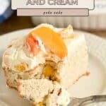 A slice of Peaches and Cream Poke Cake topped with whipped cream and fresh peach slices sits on a plate with a fork, ready to enjoy.