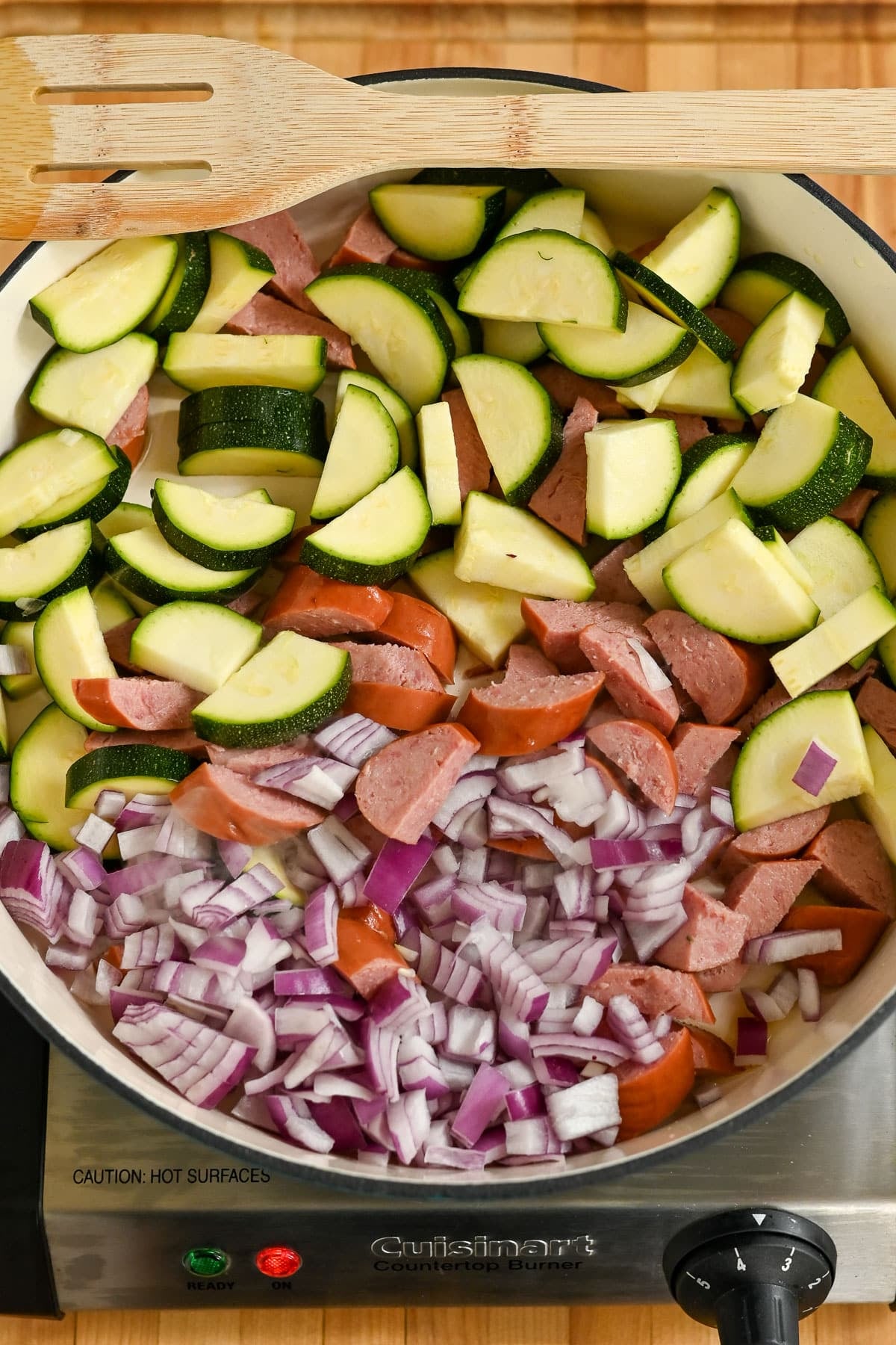 Chopped zucchini, sausage, and red onion sizzle in a pot on the stove-a perfect base for hearty Pasta with Veggies & Smoked Sausage. A wooden spatula rests beside the vibrant mixture.