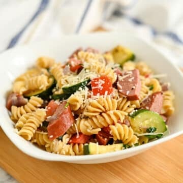 A bowl of Pasta with Veggies & Smoked Sausage featuring rotini, savory sausage, zucchini, tomatoes, and grated parmesan cheese.