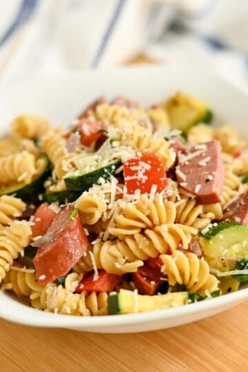 A bowl of Pasta with Veggies & Smoked Sausage featuring rotini, savory sausage, zucchini, tomatoes, and grated parmesan cheese.