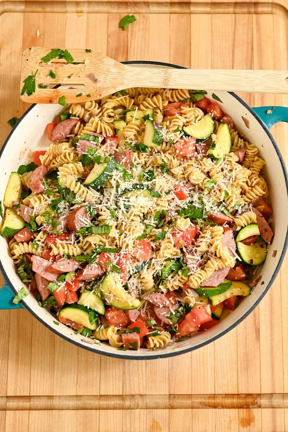 A skillet of Pasta with Veggies & Smoked Sausage-rotini pasta tossed with sausage, zucchini, tomatoes, herbs, and grated cheese-served on a rustic wooden surface.