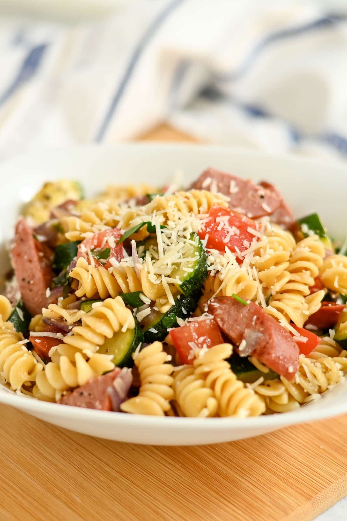 A bowl of Pasta with Veggies & Smoked Sausage features rotini tossed with sausage, zucchini, tomatoes, and a sprinkle of grated cheese on top.