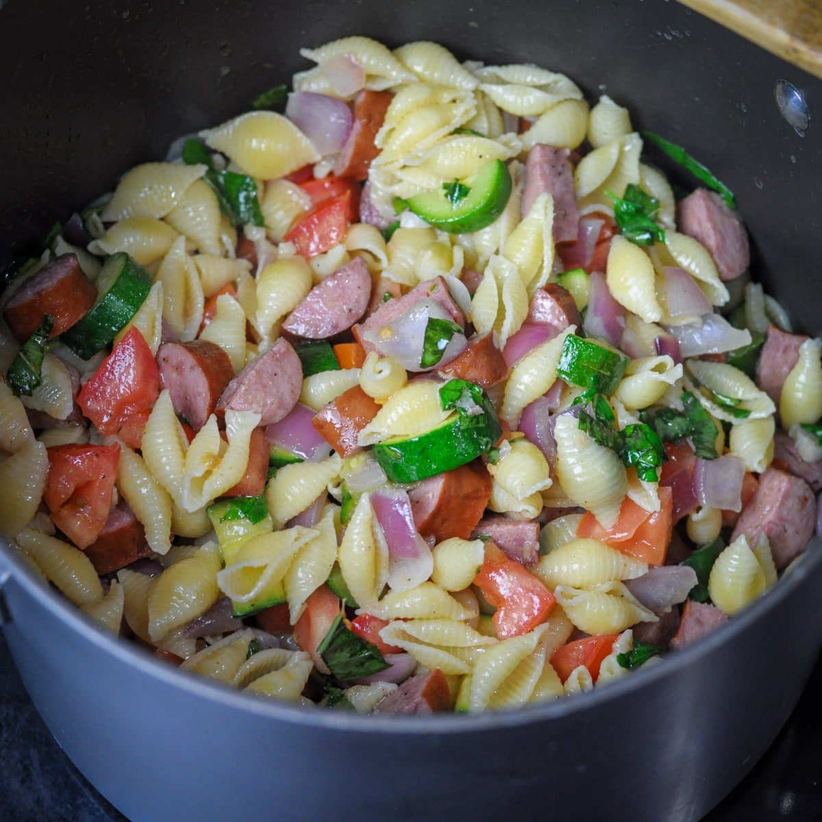 a large pot with sausage, pasta, and veggies cooking. 