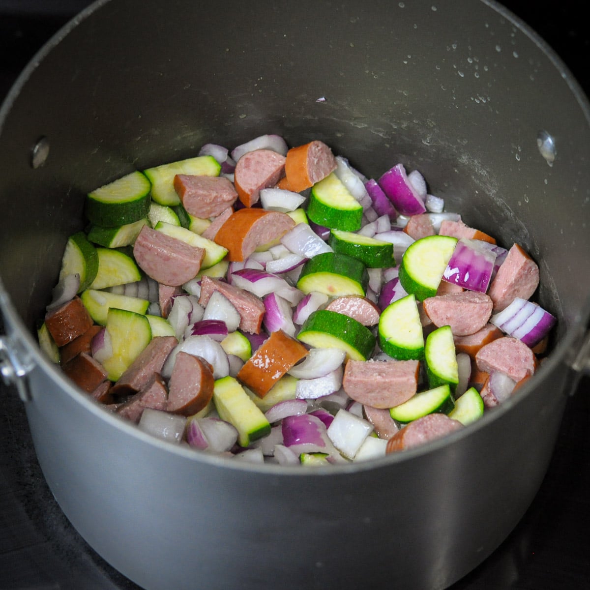 a large pot with sausage, and veggies cooking. 