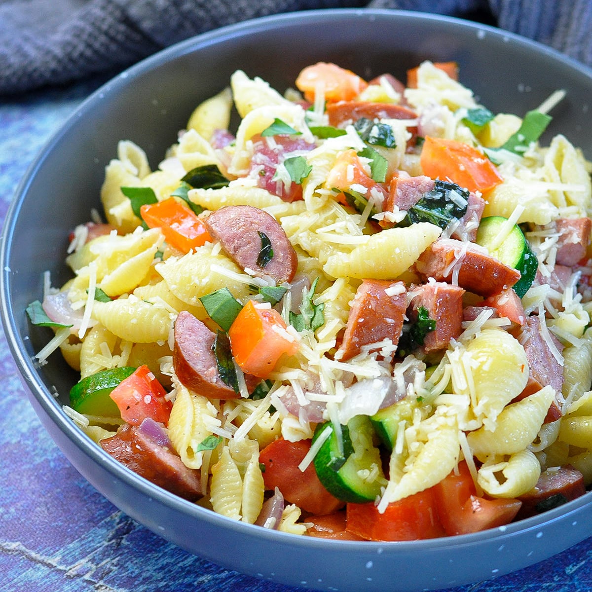 pasta with tomatoes, veggies, and sausage in a gray bowl. 