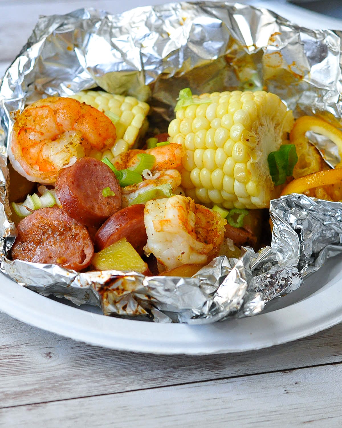 shrimp, sausage, corn, potatoes in foil ready to serve on a paper plate