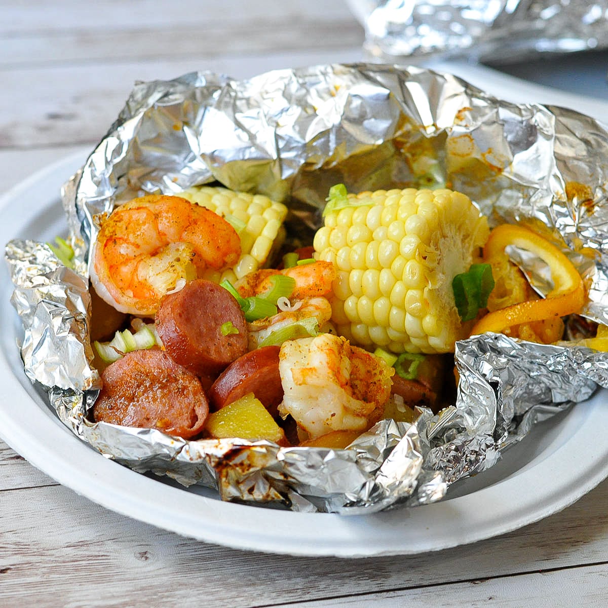 shrimp, sausage, potatoes, and corn in a foil packet sitting on a white paper plate. 