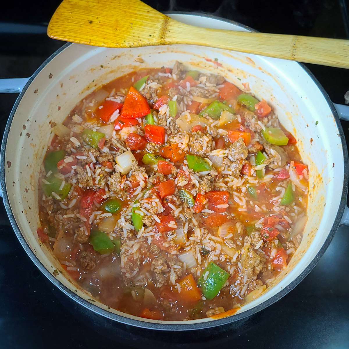 ground turkey with spices cooking in a large pot with onions, peppers, and tomatoes and rice