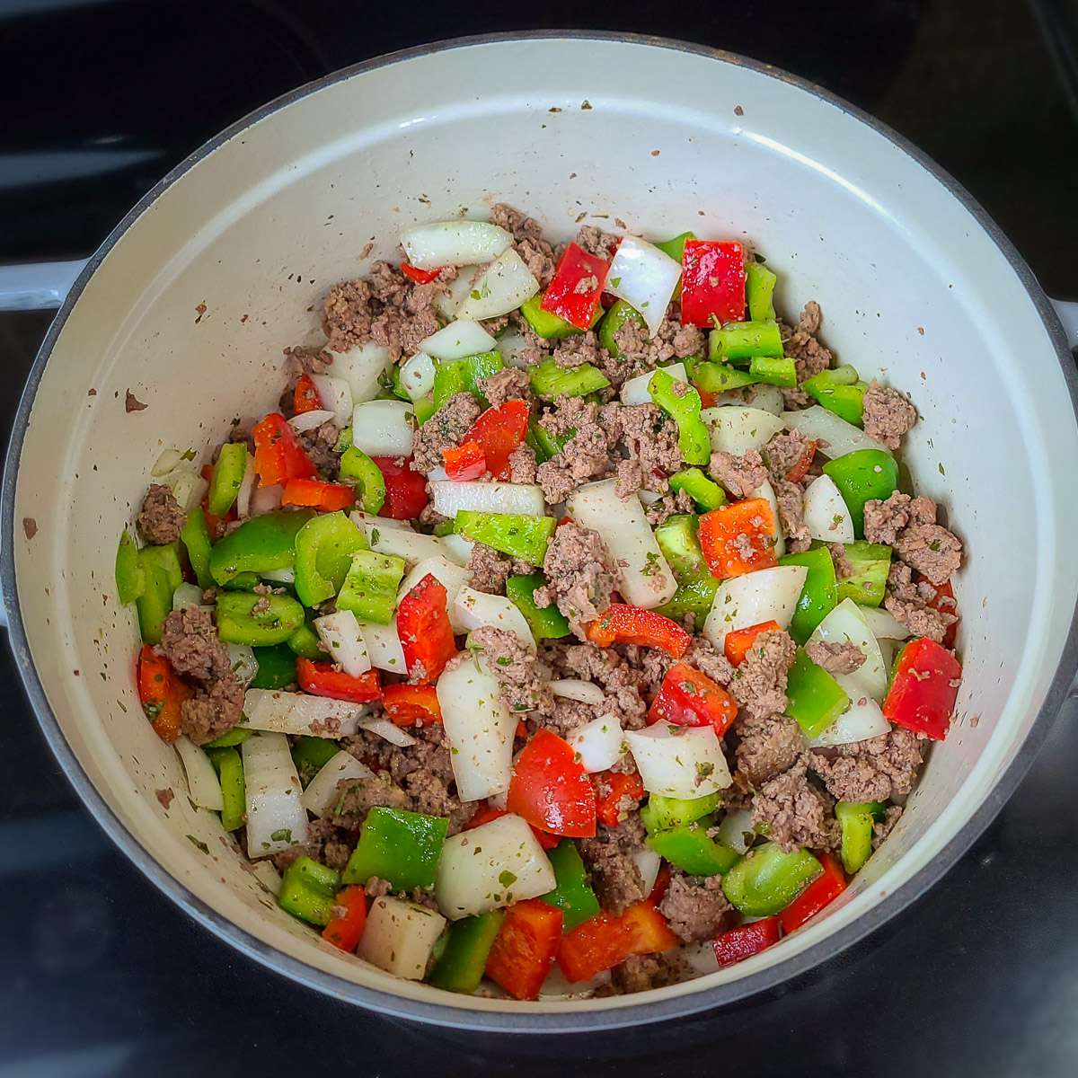ground turkey with spices cooking in a large pot with onions and red and green peppers