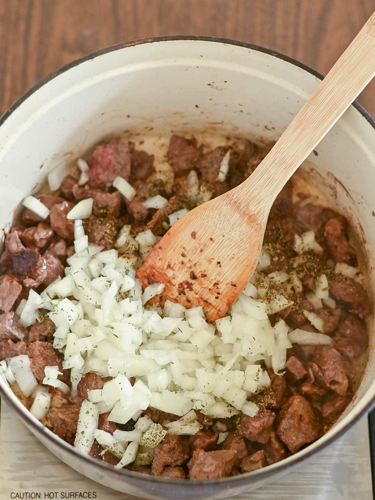 Diced onions and beef for Beef and Dumplings are being stirred in a pot with a wooden spoon.