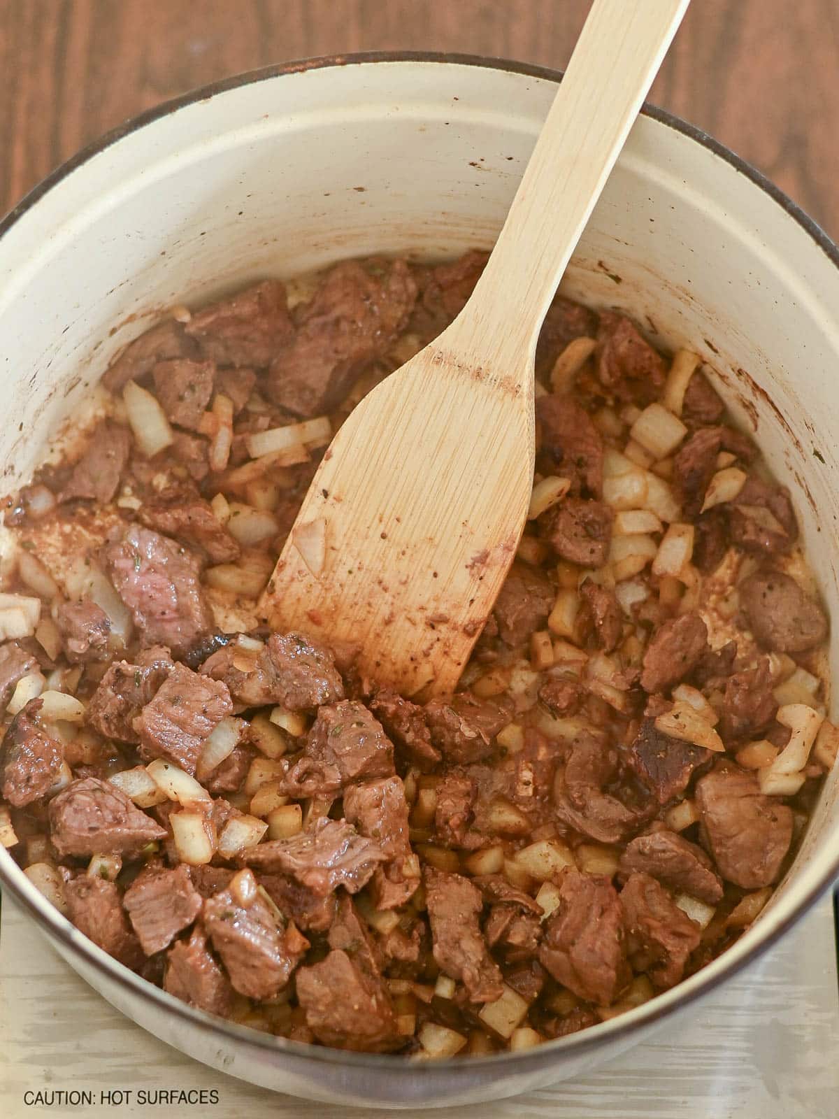 Chopped beef and diced onions are being cooked in a pot for a savory Beef and Dumplings dish, stirred gently with a wooden spatula.