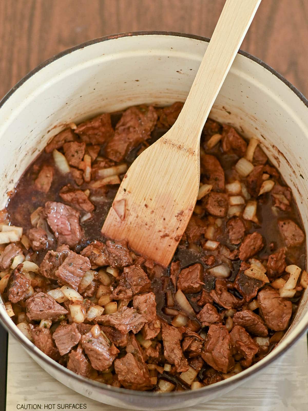 Diced beef and onions cooking in a pot, stirred with a wooden spatula-the perfect start to hearty Beef and Dumplings.