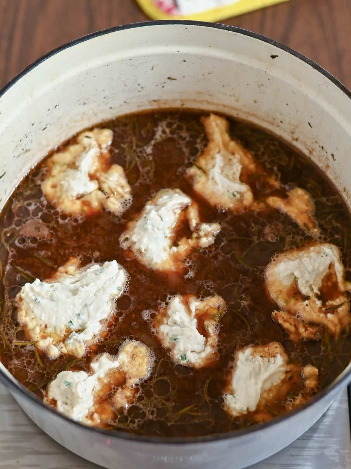 A pot of Beef and Dumplings soup with dollops of herbed dumpling dough simmering on the surface.