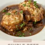 Two beef and dumplings are topped with parsley and served in a rich beef stew on a white plate.