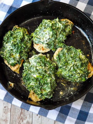 spinach and cheese covered chicken breast in a cast iron skillet