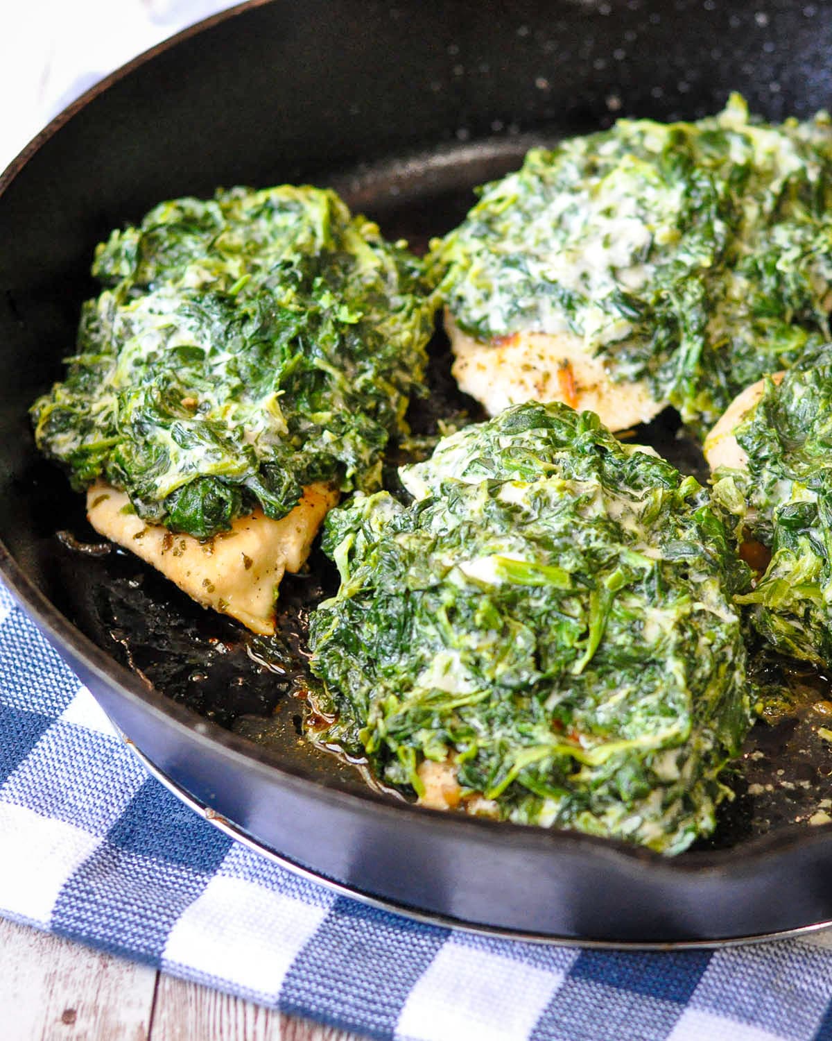 spinach and cheese covered chicken breast in a cast iron skillet
