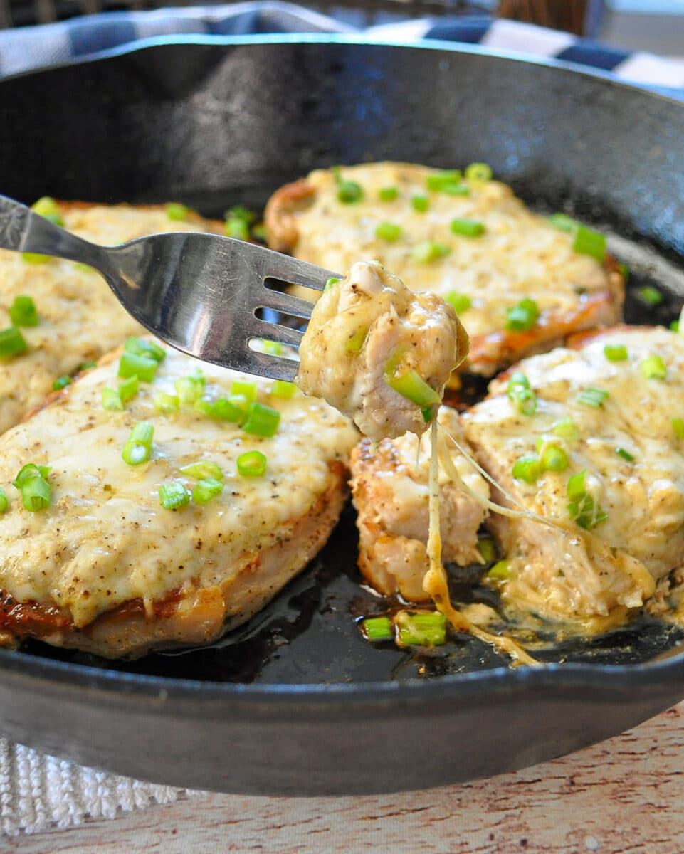 cheese topped pork chops in a skillet next to a blue and white towel