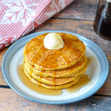 a stack of pumpkin spice pancakes with butter and syrup with a fall themed towel in the back ground