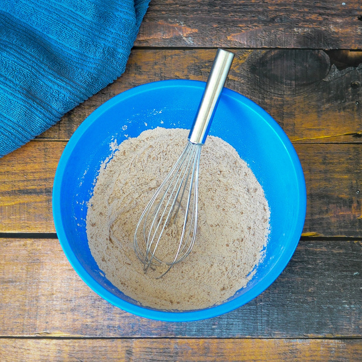 flour and cocoa powder in a blue bowl with a metal whisk