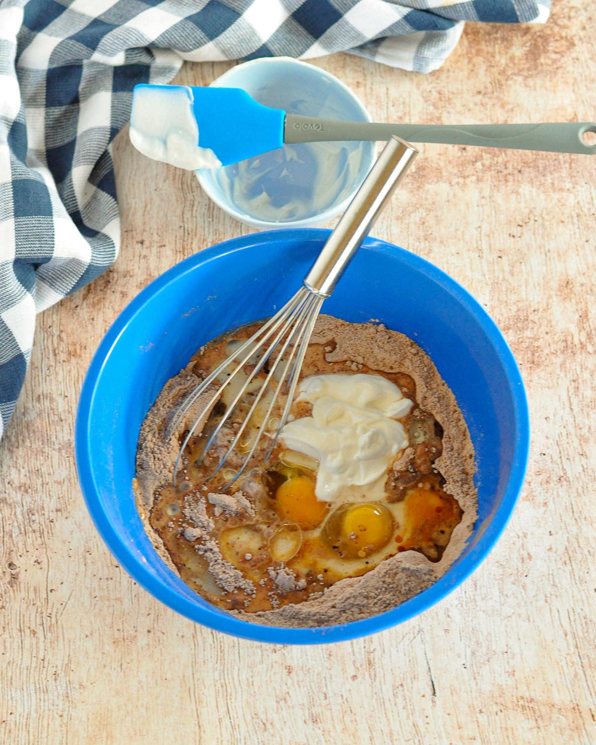 A blue bowl with a whisk, eggs, and other ingredients to make muffin batter.