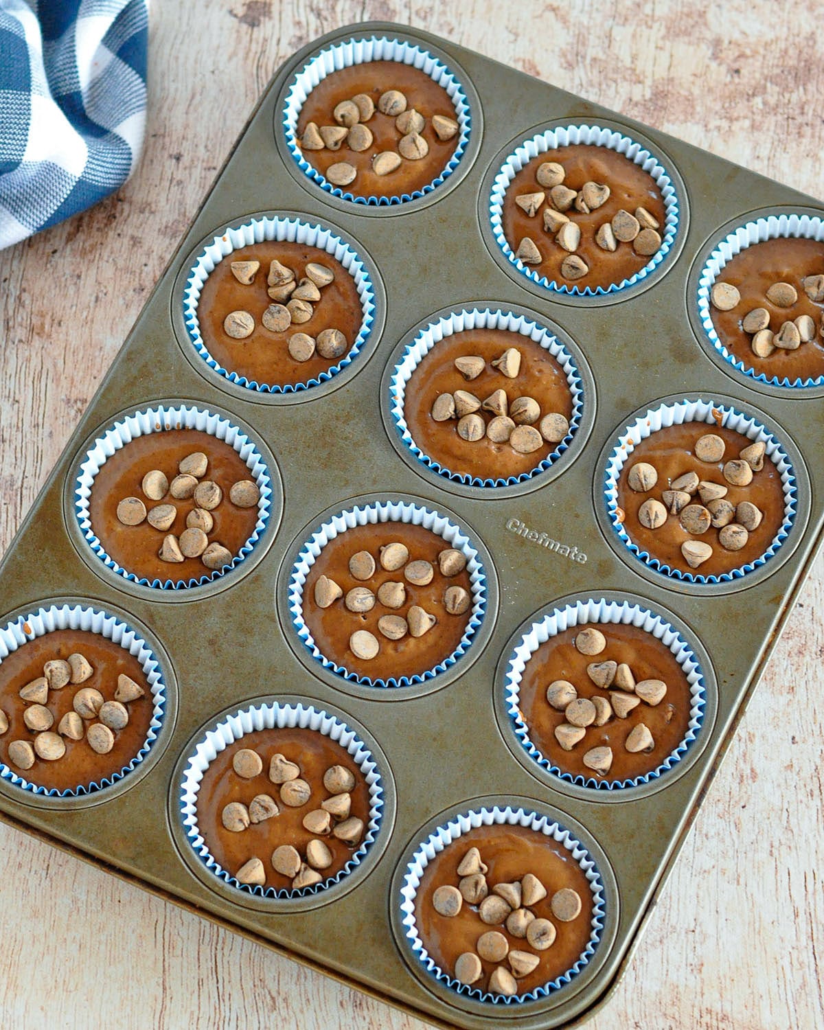 Chocolate chips topped onto chocolate muffin batter in a muffin tin ready to bake.