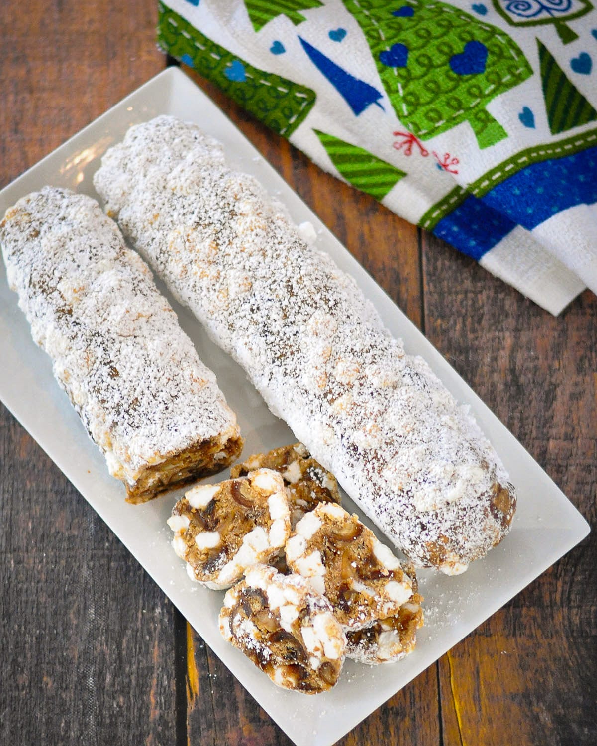 two powdered sugar covered date rolls on a white rectangle platter. 