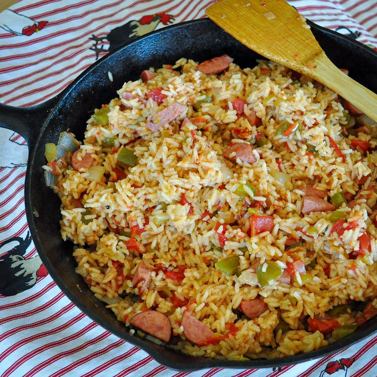 a cast iron skillet filled with jambalaya sitting on a rooster print apron