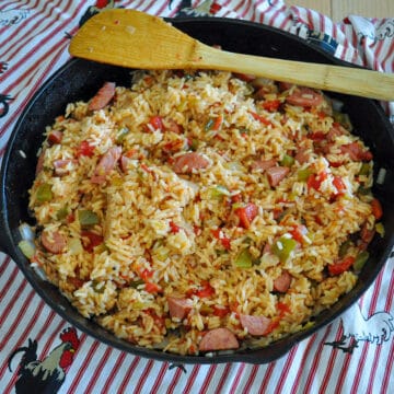 a cast iron skillet filled with jambalaya sitting on a rooster print apron